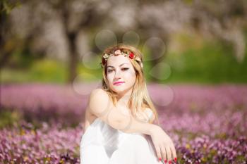 Young beautiful romantic blonde woman in white dress in blooming garden.