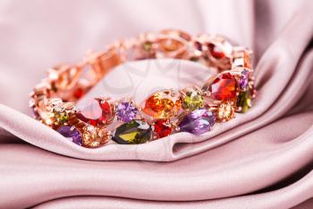 Stylish bracelet with colorful stones on fabric background.