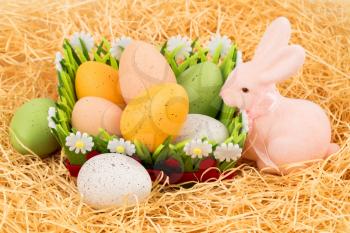Easter colorful eggs in basket and pink bunny on straw background.