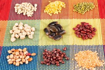 The collection of different beans on the colorful bamboo placemat.