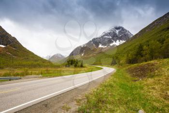 Landscape with high rocky mountains, road and trees in Lofoten islands, Norway.