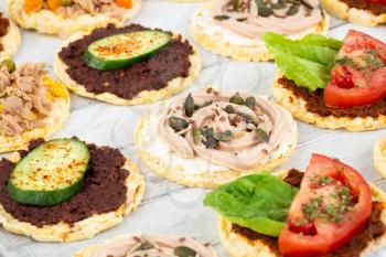 Quinoa crackers with olive and sundried tomatoes paste, tuna fish and vegetables on gray wooden background.