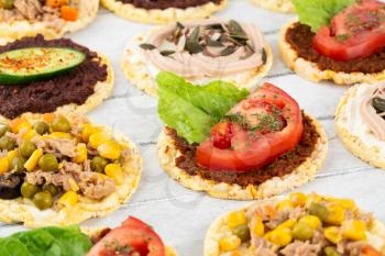 Quinoa crackers with olive and sundried tomatoes paste, tuna fish and vegetables on gray wooden background.