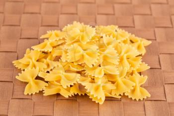 The heap of farfalle pasta on the brown bamboo place mat.