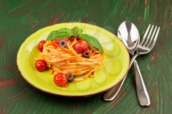 Pasta spaghetti Napoli or Napolitana on green plate with fork and spoon on colorful background. Italian cuisine.