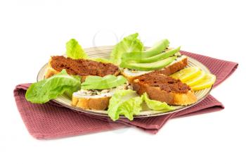 Sandwiches with cheese, sundried tomatoes, avocado and seeds, lettuce, lemon on beige  plate on towel isolated on white background.
