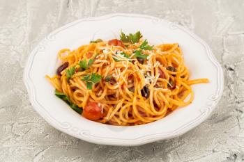 Pasta spaghetti Puttanesca on white plate on gray background. Italian cuisine.