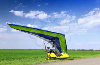 Motorized hang glider over green grass, ready to fly.