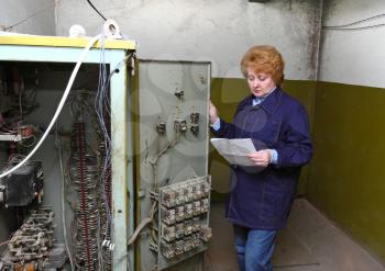 Operator woman-engineer in machine room (elevator) check the mechanical relay and cabinet.