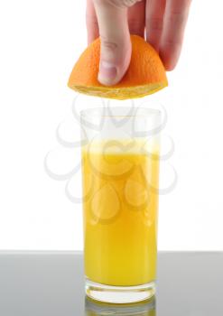 Glass of orange juice with hand, squeeze of orange.