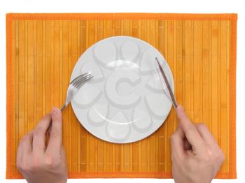 Hands hold fork and knife above plate on bamboo mat. All around Isolated.