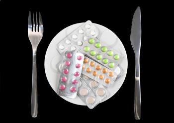 Coloured pills in white plate with fork and spoon , on black background.