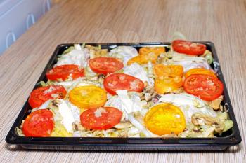 Raw chiken on baking tray with tomato and potato.