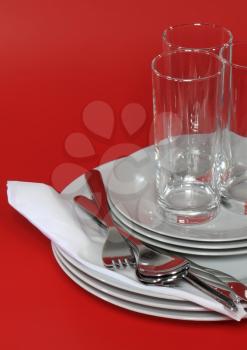 Pile of white plates, glasses with forks and spoons on silk napkin. Red background