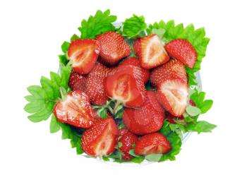 A heap of fresh strawberries in glass bowl on green foliage . Isolated