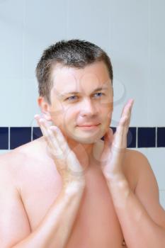 A young man uses a lotion after shaving in bathroom.