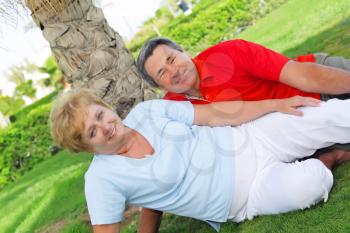 Mature couple lying on the green lawn near the palm in tropican resort.