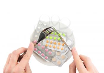 Coloured pills in white plate with fork and spoon in hands, on white background. Isolated