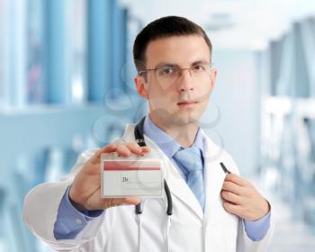 Friendly medical doctor with blank card (badge) in Hospital.