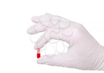 Hand holding a capsule or pill in medical gloves, on white background.