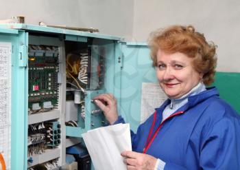 Operator woman-engineer in machine room (elevator) near electronic cabinet.