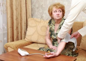 Old woman measures arterial pressure , with doctor helps.
