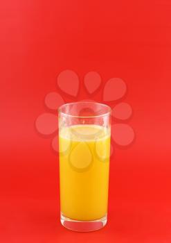 Glass of fresh orange juice with squeeze slice on red background.