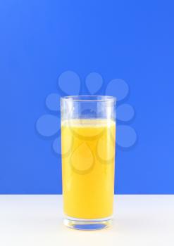Glass of fresh orange juice with squeeze slice on blue background.