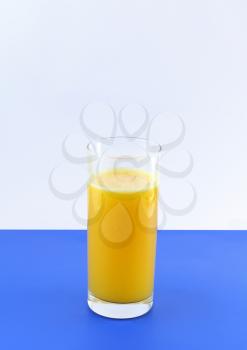 Glass of fresh orange juice with squeeze slice on blue background.