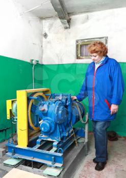 Operator woman-engineer in machine room (elevator) check the mechanical equipment.