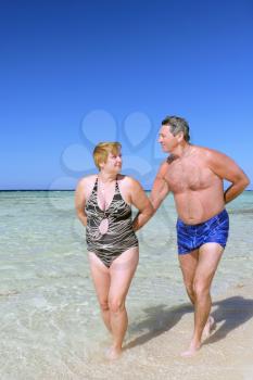 Mature couple walking on the beach in tropical resort.