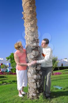 Mature couple near palm-tree  looked at each other with love. In tropical resort.