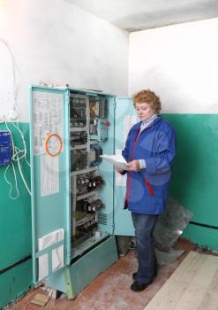 Operator woman-engineer in machine room (elevator) near electronic cabinet.