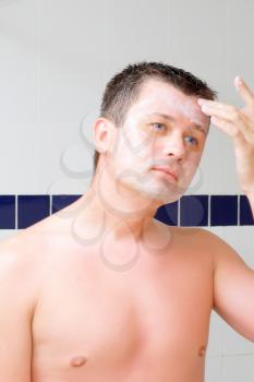 A young man puts on face cream mask in bathroom.