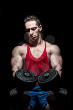young bodybuilder posing with dumbbell at the bench on black background