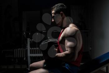 young bodybuilder resting at the bench on black background