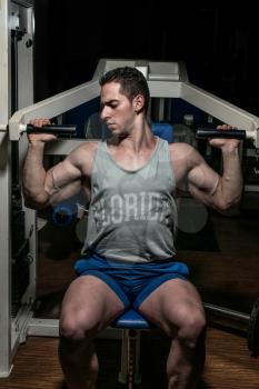 young bodybuilder doing shoulder press on machine