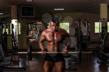 bodybuilder doing heavy weight exercise for biceps with barbell