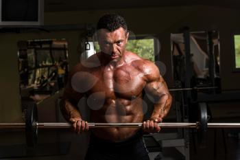 bodybuilder doing heavy weight exercise for biceps with barbell