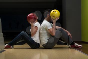 Young Couple Hiding Their Faces Behind Bowling Ball