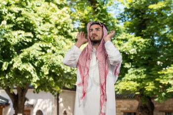 Young Muslim Man Making Traditional Prayer To God While Wearing A Traditional Cap Dishdasha