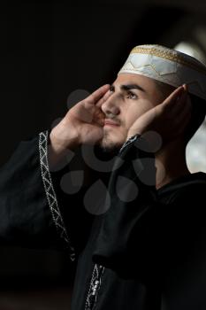Young Muslim Guy Making Traditional Prayer To God While Wearing A Traditional Cap Dishdasha