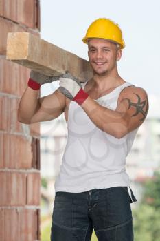Smiling Carpenter Carrying A Large Wood Plank On His Shoulder