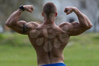 Bodybuilder Performing Rear Double Biceps Poses In Park