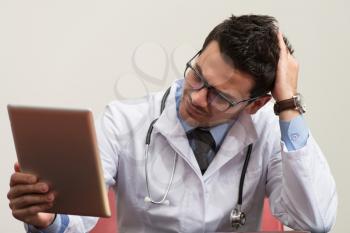 Stressed Out Doctor With Hands Clasped Sitting At Table In Conference Room