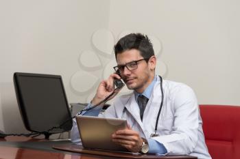 Young Doctor Working At His Computer While Talking On The Phone