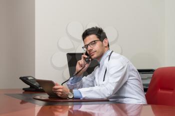 Young Doctor Working At His Computer While Talking On The Phone
