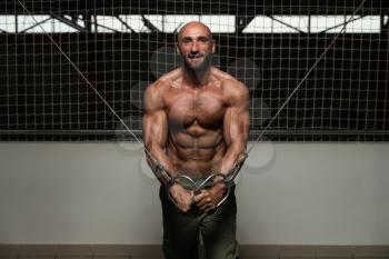 Mature Bodybuilder Is Working On His Chest With Cable Crossover In A Dark Gym