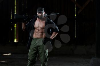 Action Hero Muscled Man Holding Machine Gun - Standing In Abandoned Building Wearing Green Pants