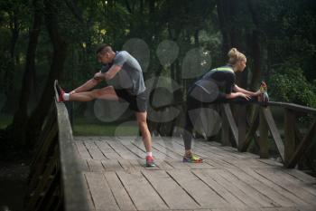 Young Couple Stretching Before Running In Wooded Forest Area - Training And Exercising For Trail Run Marathon Endurance - Fitness Healthy Lifestyle Concept